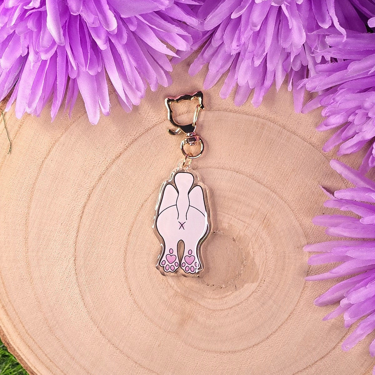 cat butt keychain on a wooden surface with purple flowers