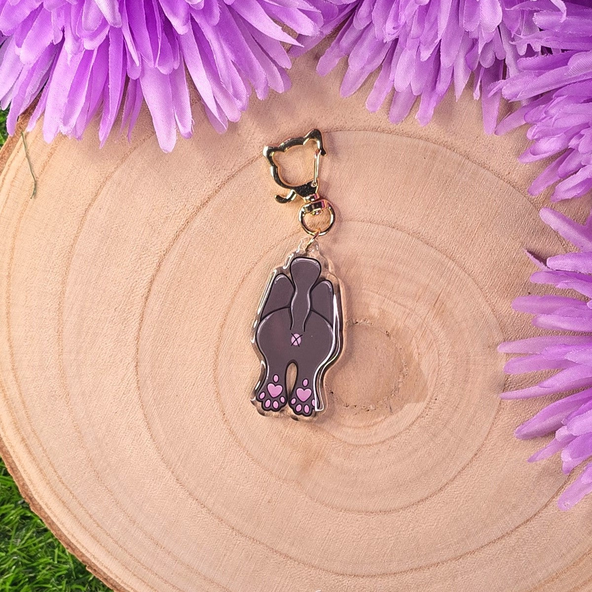 Keychain on a wooden surface surrounded by purple flowers.