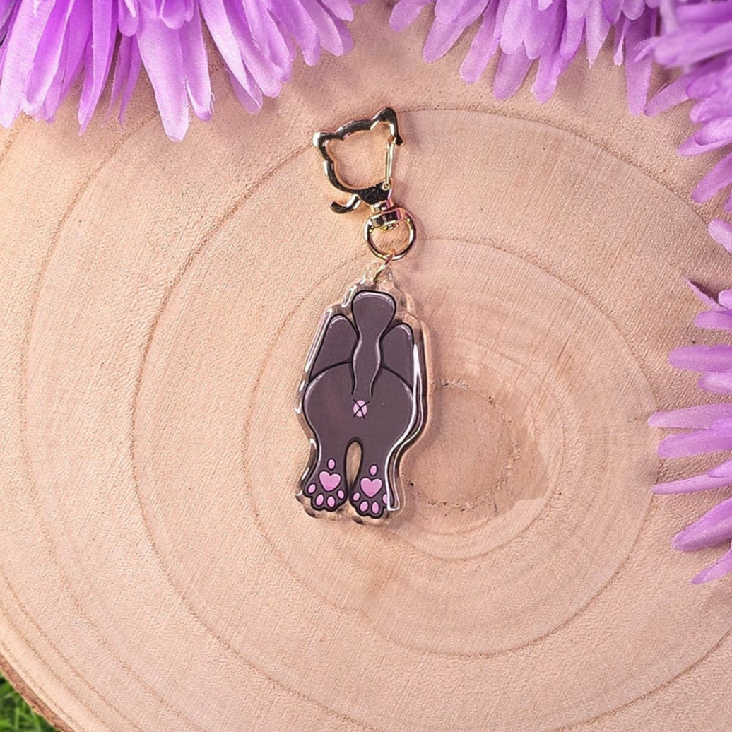 cat butt -shaped keychain on a wooden surface with purple flowers around