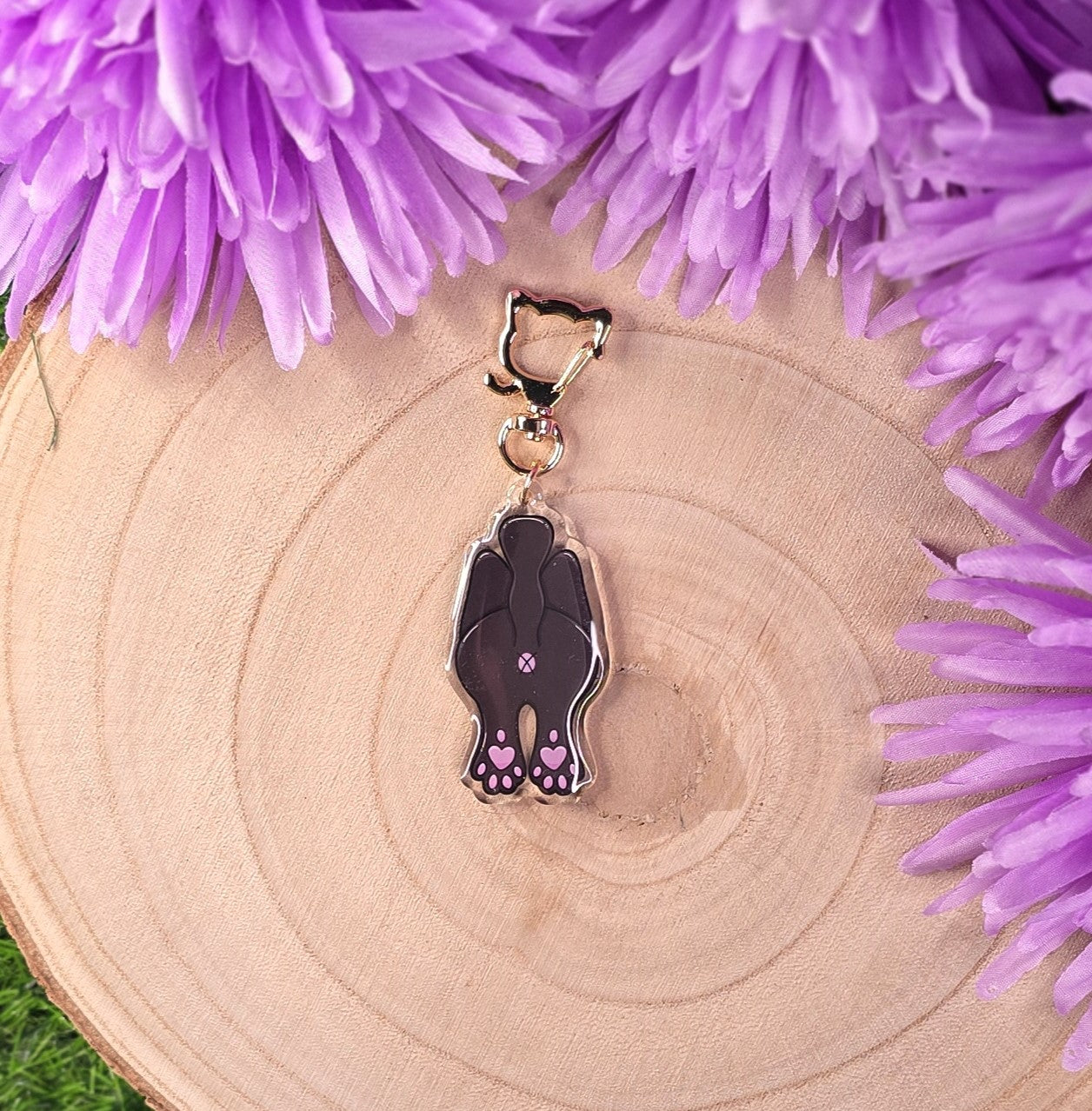 Keychain with a design of cat butt on a wooden surface with purple flowers.