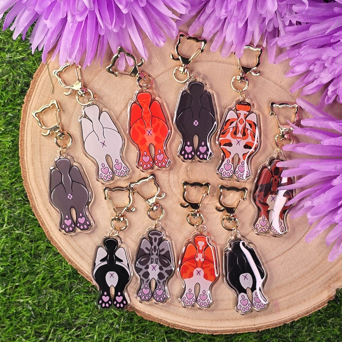Set of colorful cat-shaped keychains on a wooden board with purple flowers in the background.