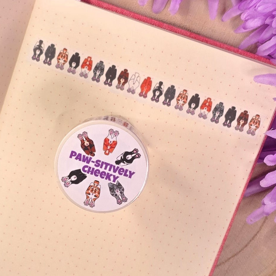 washi tape with cat buts on, resting on a book with purple flower in the background.