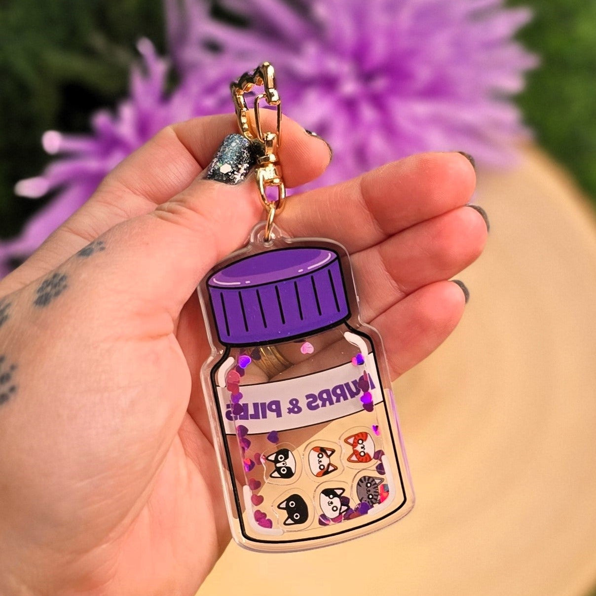 Hand holding a keychain with a purple bottle design against a blurred natural background
