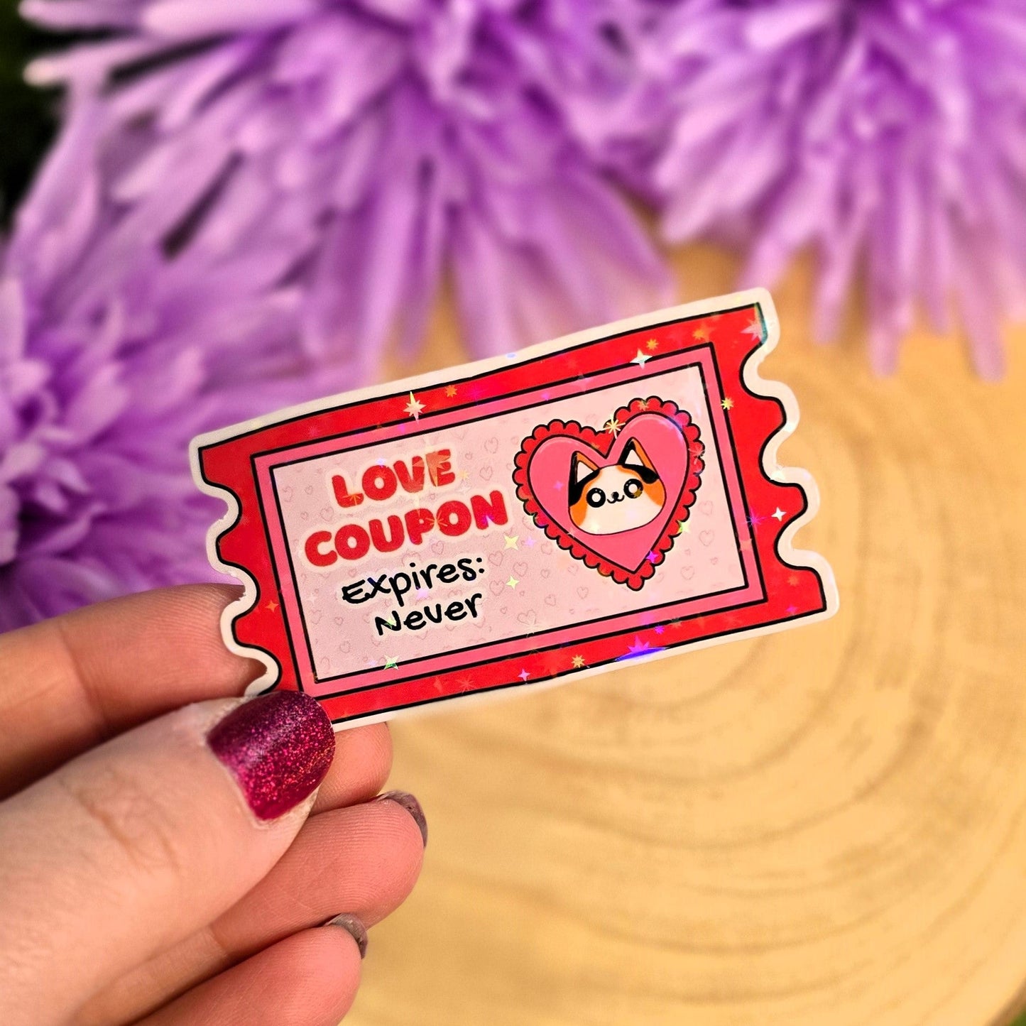 Hand holding a 'Love Coupon Expires: Never' sticker with purple flowers in the background