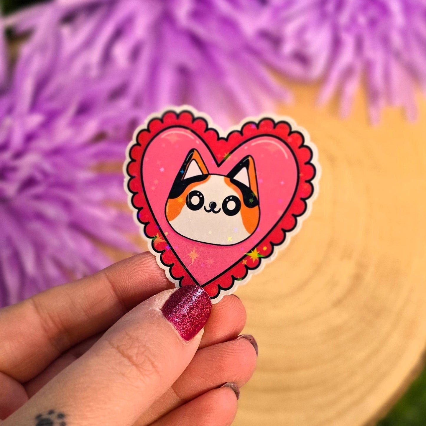 Heart-shaped sticker with a cartoon character held by a hand against a blurred purple flower background