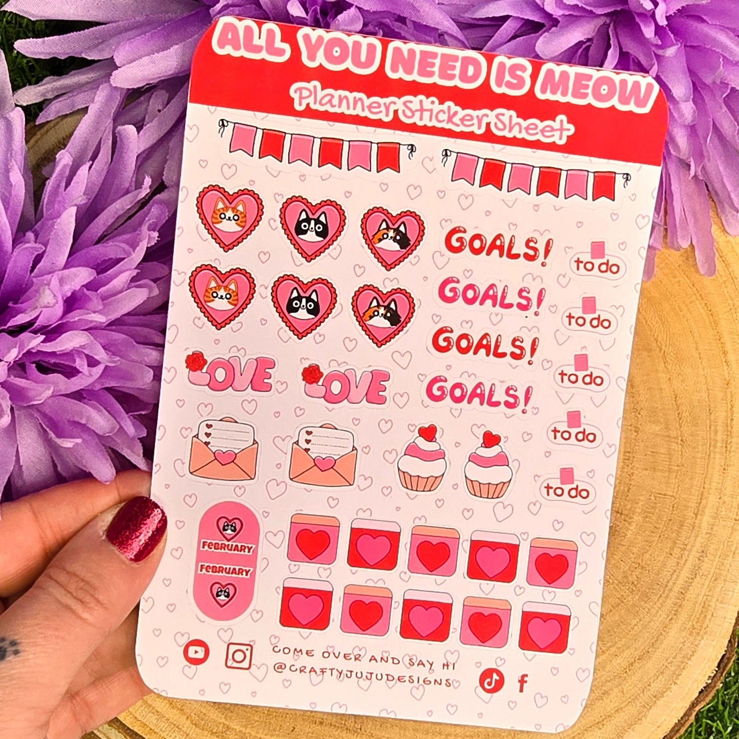 Sheet of stickers with 'All You Need is Meow' text held over purple flowers on grass.