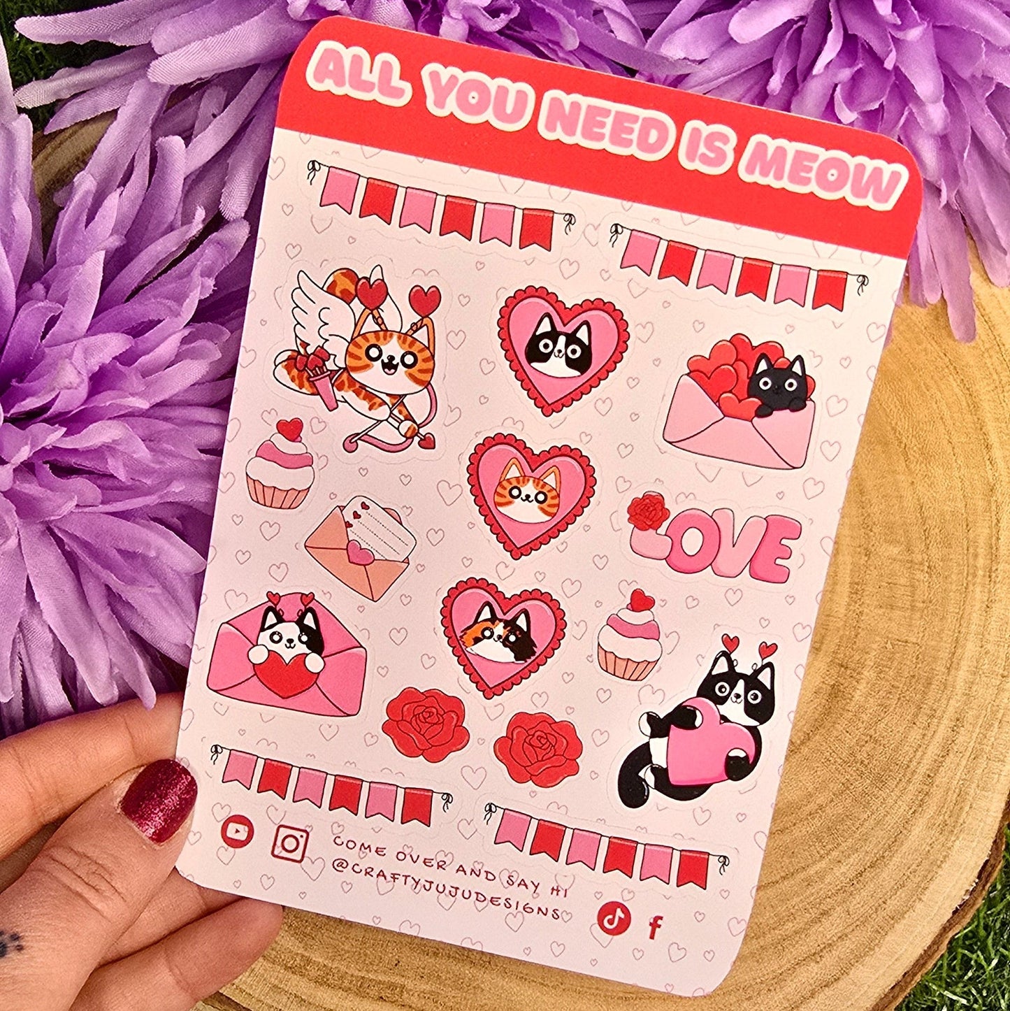 Sticker sheet with cat-themed designs held over purple flowers on grass
