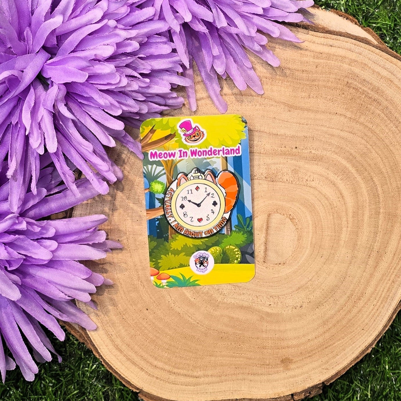 enamel pin with a clock design on a card on a wooden log surrounded by purple flowers