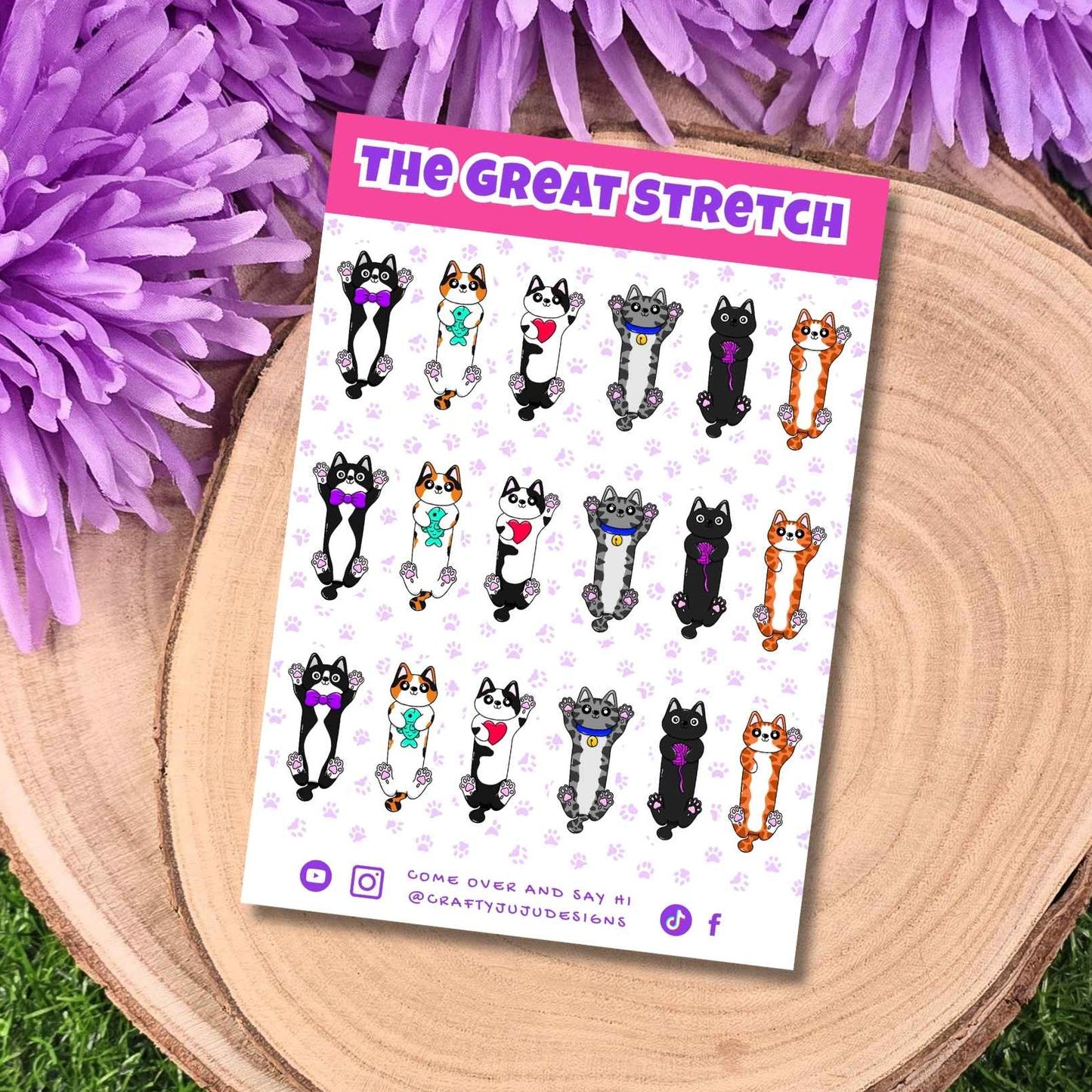A sticker sheet titled 'THE GREAT STRETCH' featuring cartoon cat illustrations in various poses, displayed on a round wooden slice with purple flowers around it.