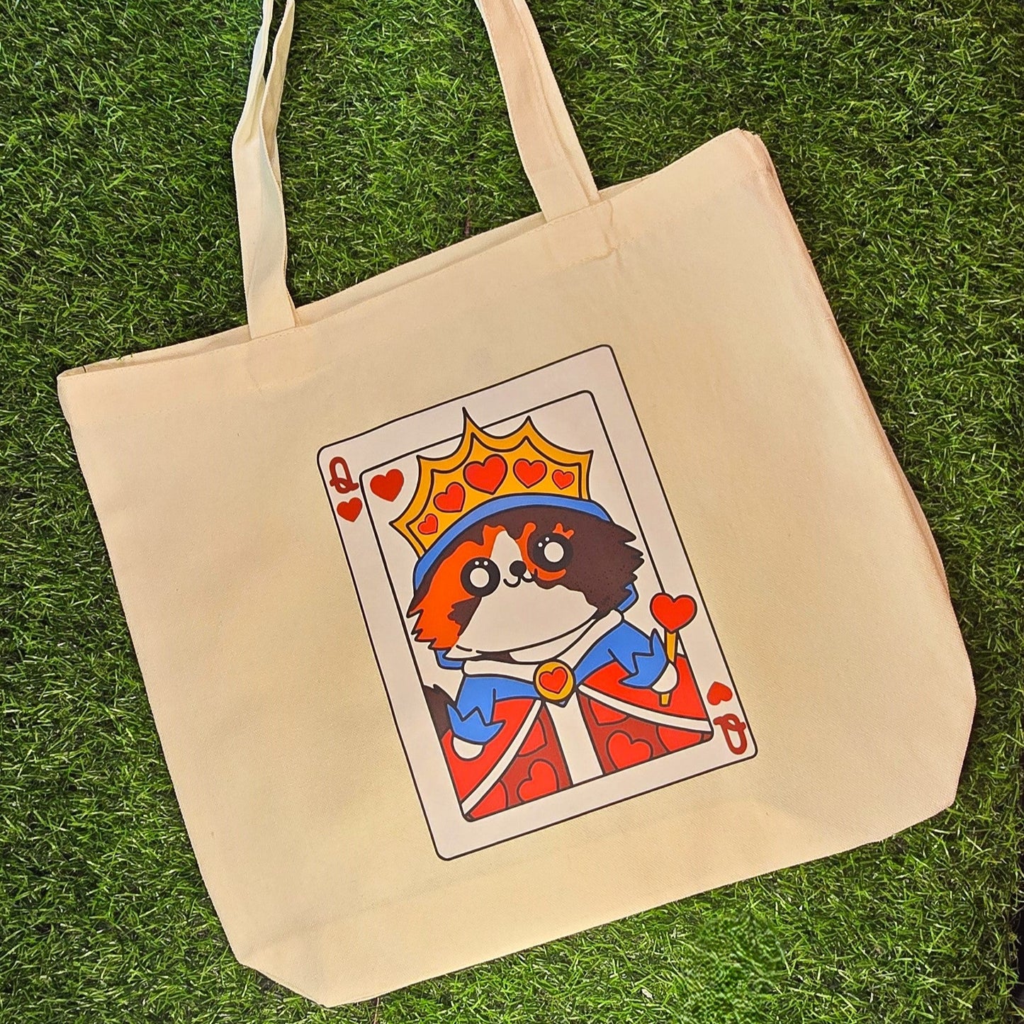Beige tote bag with a card-themed design featuring a cat in a king's outfit on grass.