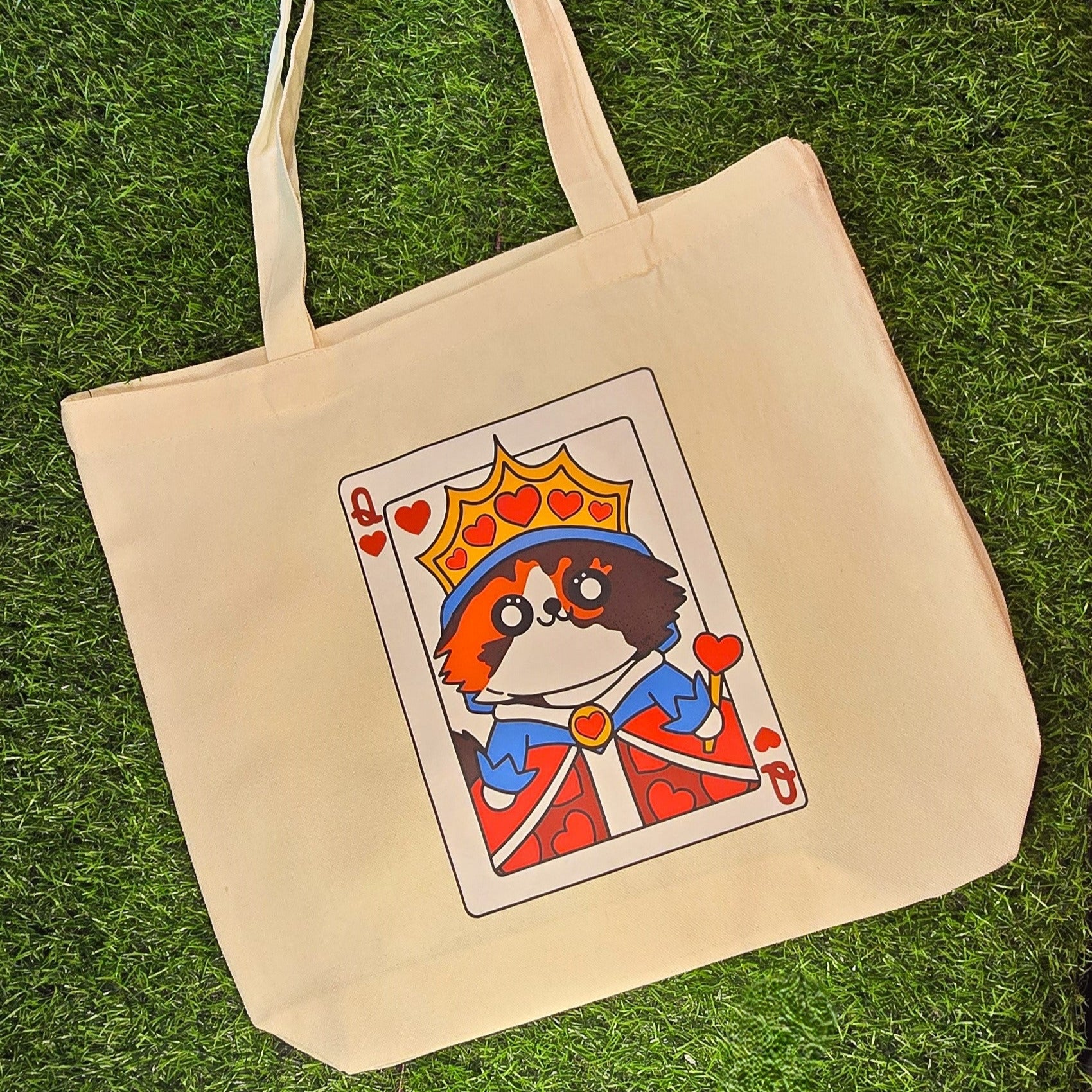 Beige tote bag with a card-themed design featuring a cat in a king's outfit on grass.