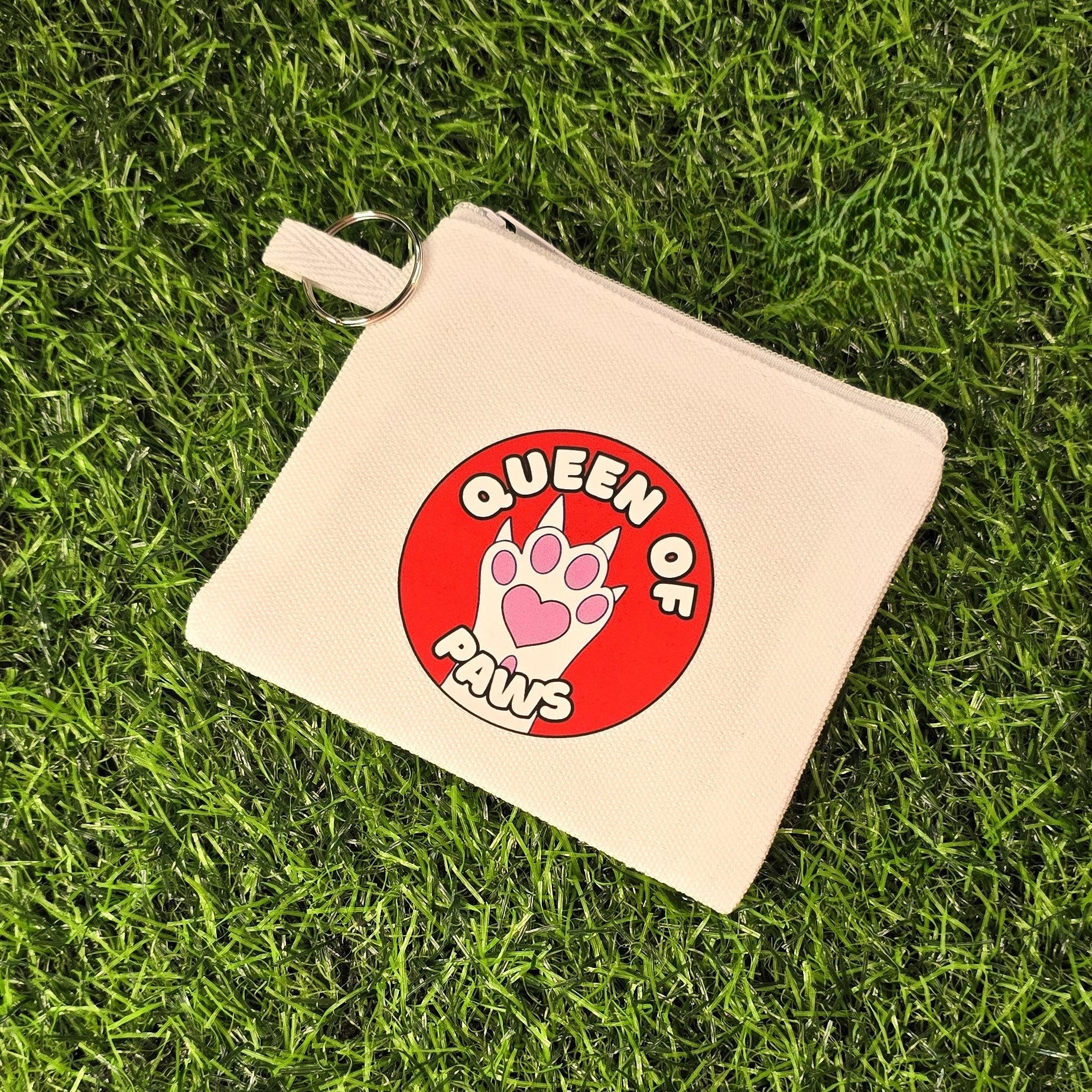 Beige pouch with 'Queen of Paws' design on a grass background