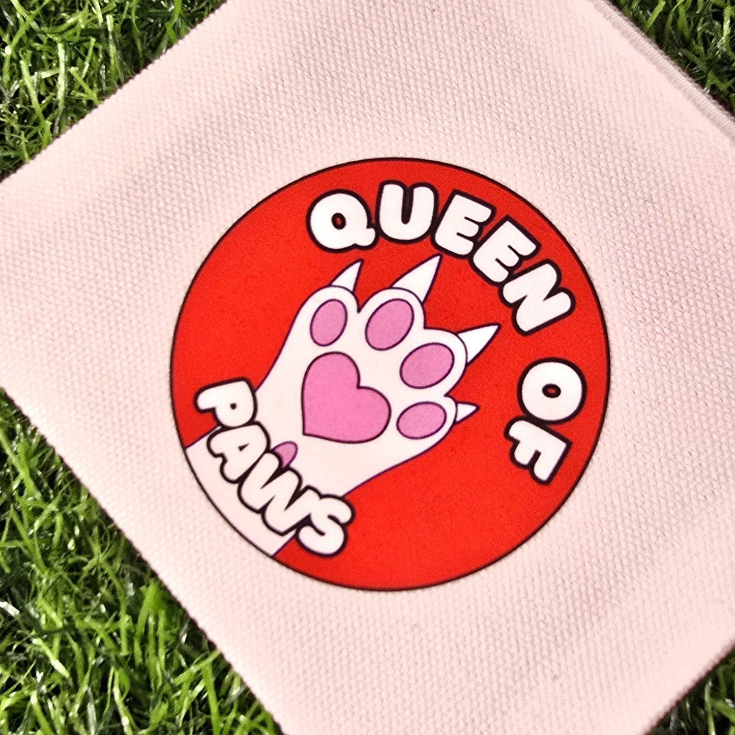 cream pouch with 'Queen of Cats' design on a grass background