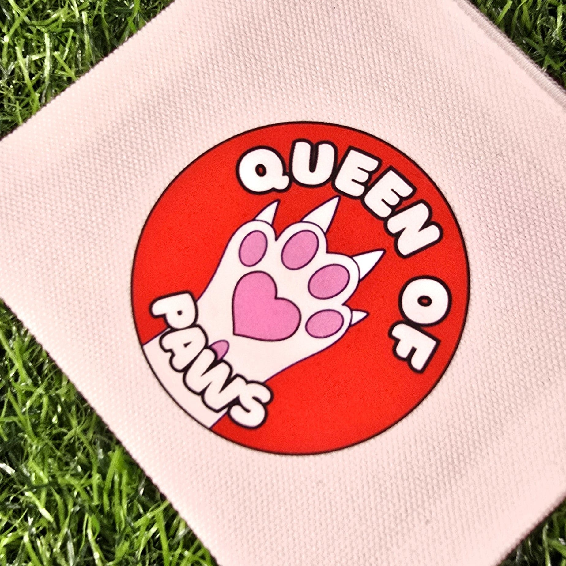 cream pouch with 'Queen of Cats' design on a grass background