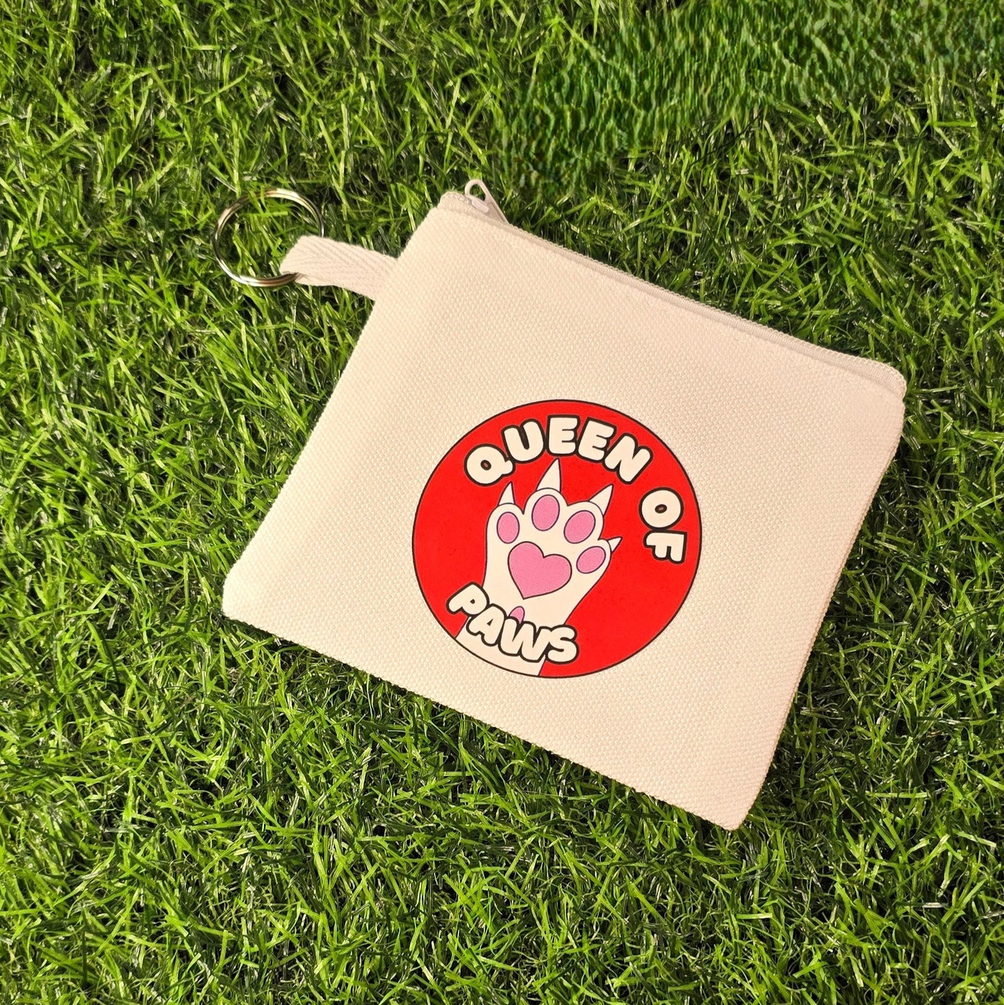 Beige pouch with 'Queen of Paws' design on a grass background