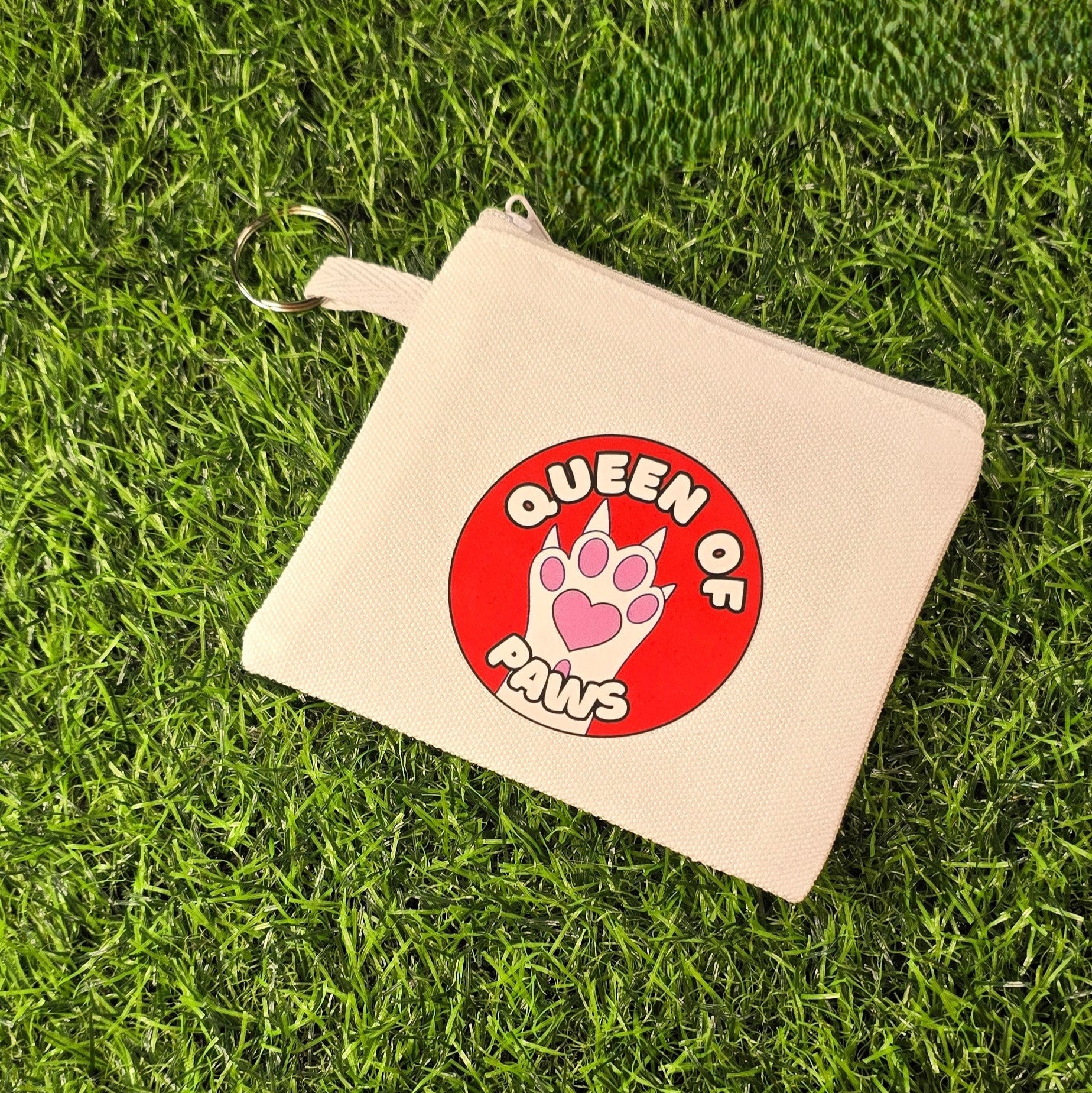 Beige pouch with 'Queen of Paws' design on a grass background