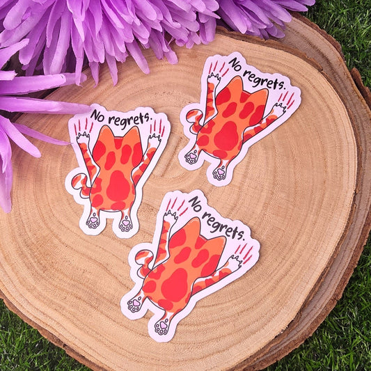 Three stickers of a red creature with 'No regrets' text on a wooden surface with purple flowers in the background.