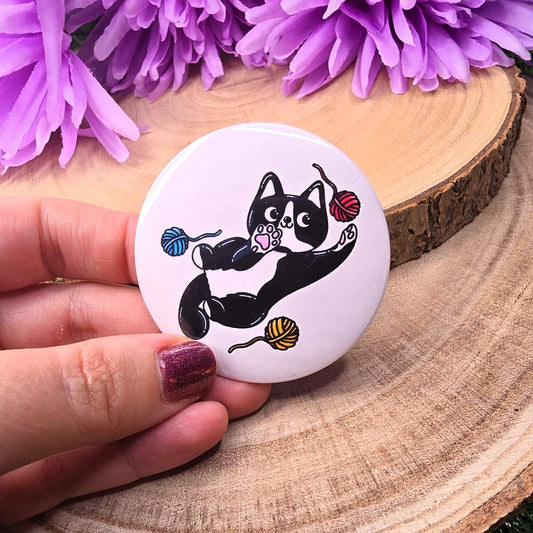 Circular product with a cat design held by a hand on a wooden surface with purple flowers in the background