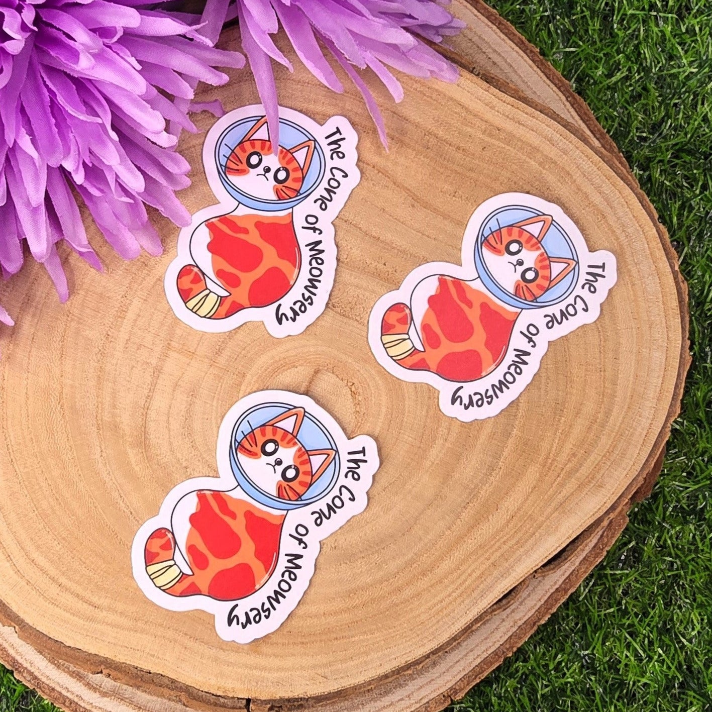 Four stickers with a cat design on a wooden surface with purple flowers.