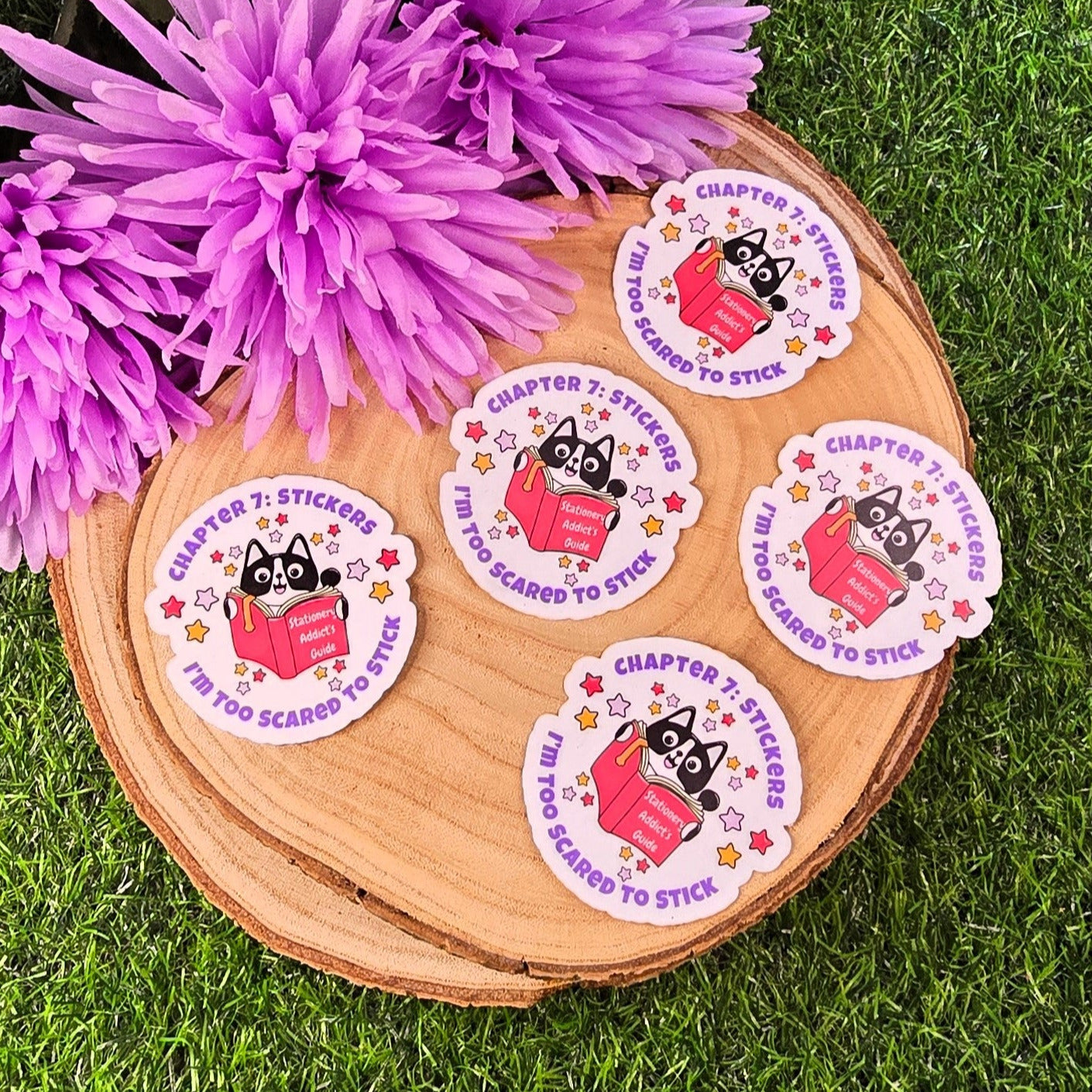 Set of stickers with a cat design on a wooden board with purple flowers in the background.