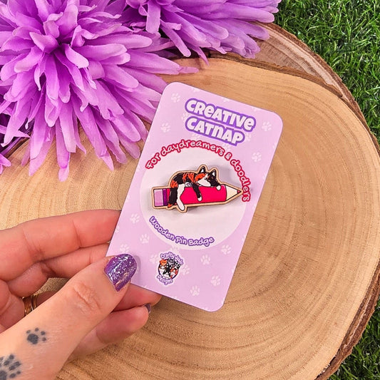 Hand holding a 'Creative Catnap' badge card with purple flowers in the background 