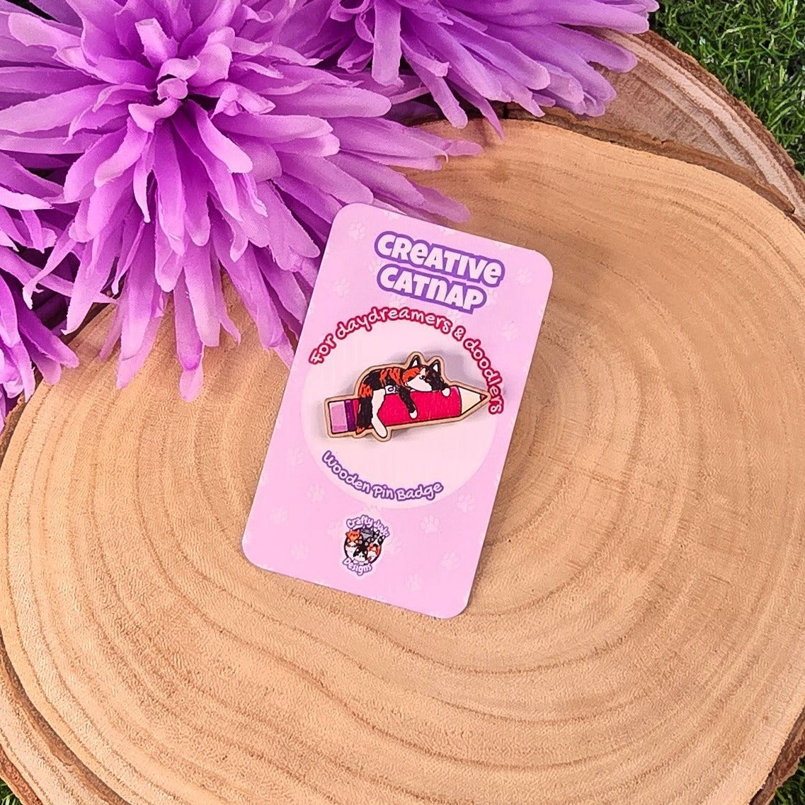 Purple flowers on a wooden surface with a pink card featuring cartoon characters.