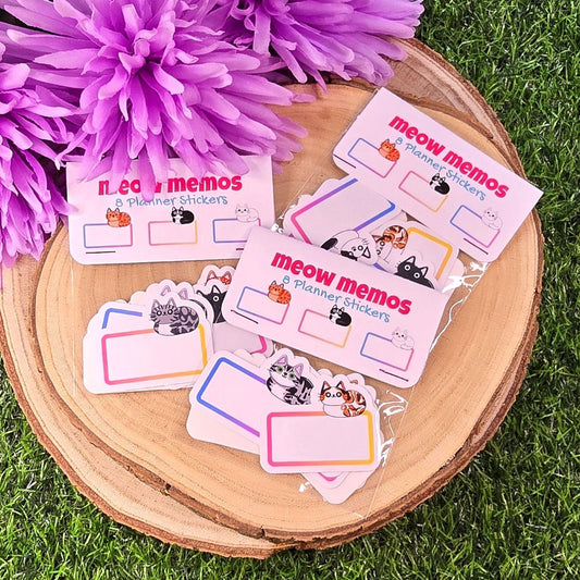 Meow Memos planner stickers on a wooden surface with purple flowers in the background
