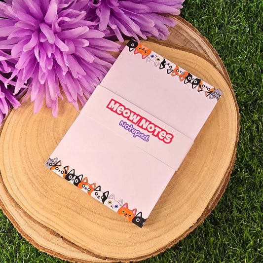Notebook titled 'Meow Notes' on a wooden surface with purple flowers in the background