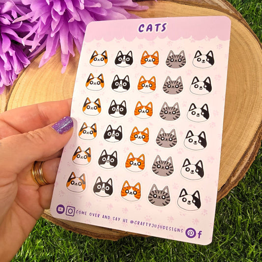 Sheet of cat-themed stickers held over a purple flower and grass background