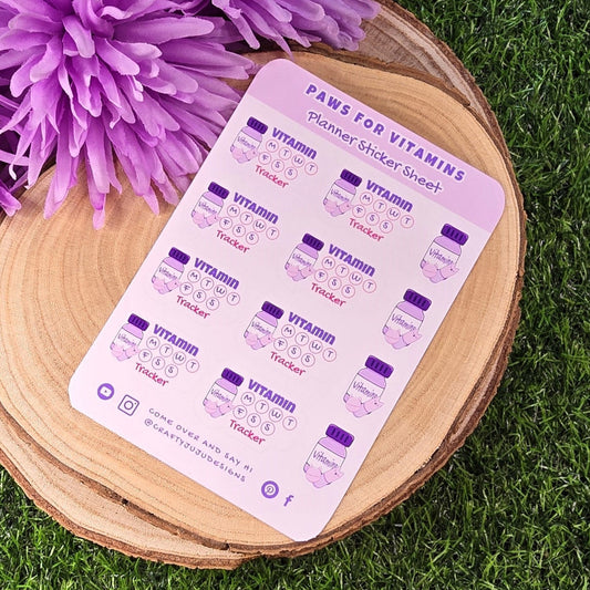 planner sticker sheet with 'Paws for Vitamins' on a wooden stand with purple flowers on grass