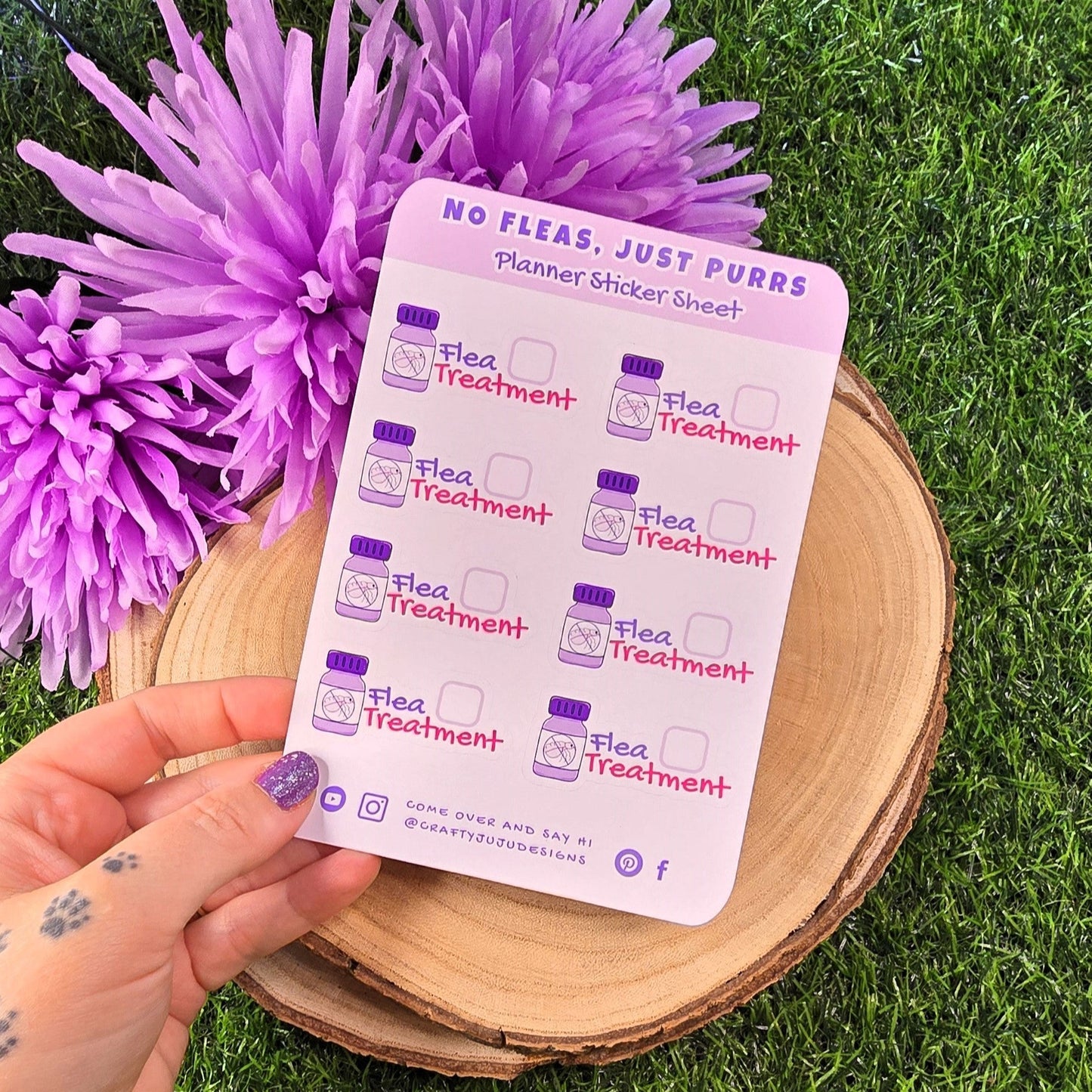 Planner sticker sheet with 'Flea Treatment' design held over purple flowers on grass