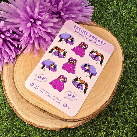Sheet of stickers with cat illustrations on a wooden coaster with purple flowers in the background