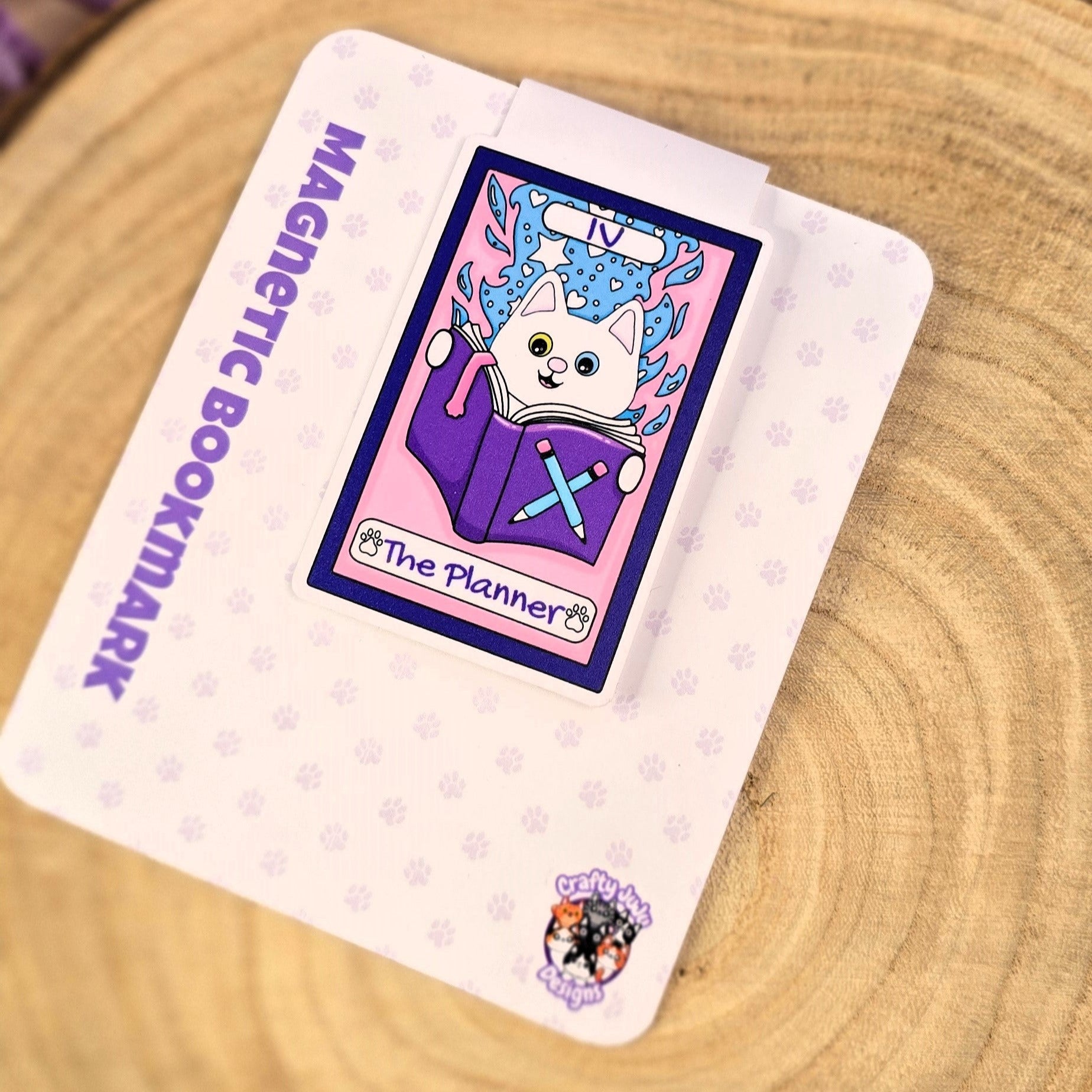 Magnetic bookmark with cartoon cat design on a wooden surface with purple flowers.
