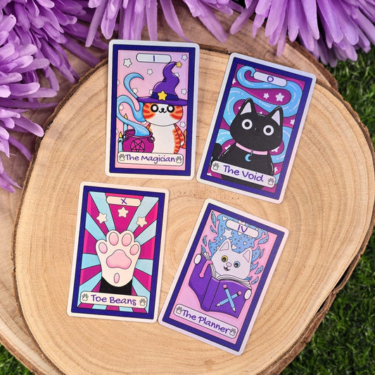 Four colorful sticker tarot cards on a wooden surface with purple flowers in the background