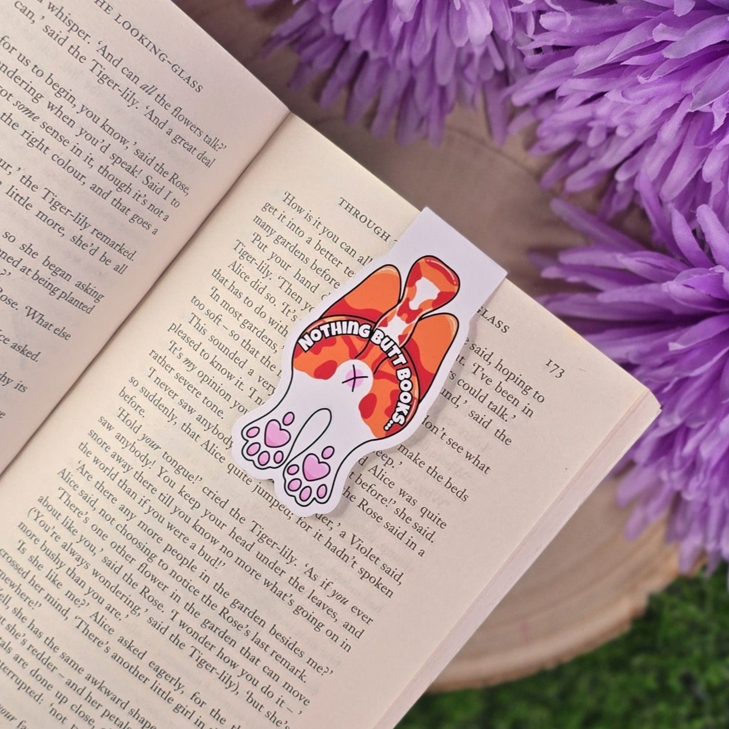 Open book with a bookmark featuring a cat butt, surrounded by purple flowers.