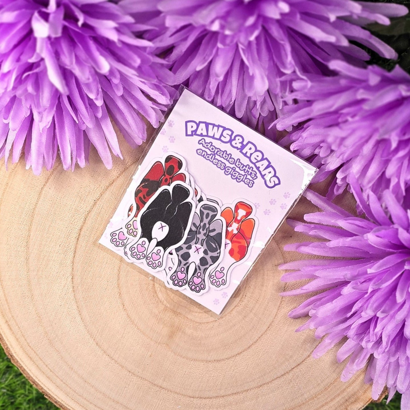 Sticker pack with cats showing off their butts illustrations on a wooden log with purple flowers in the background
