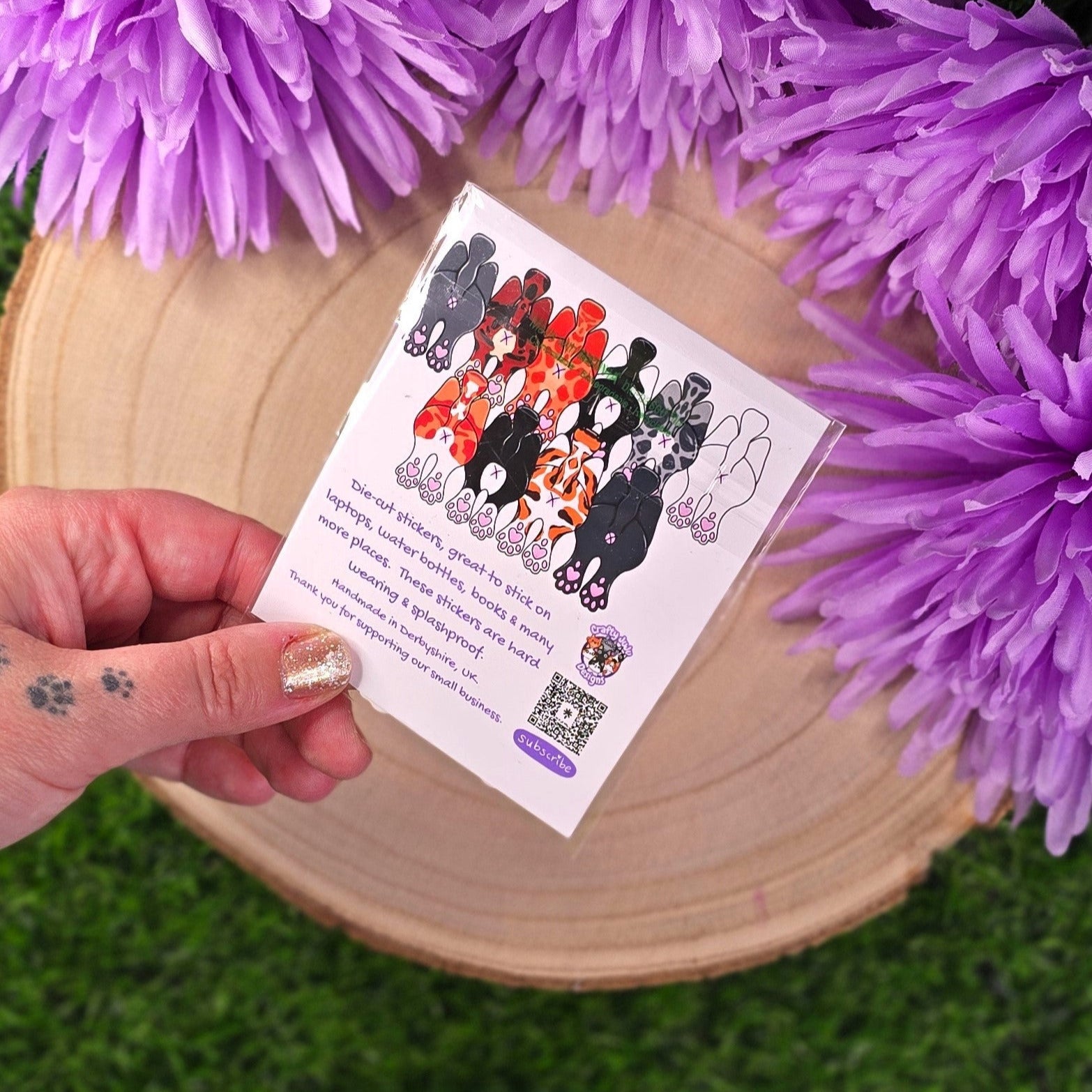Sticker pack with cats showing off their butts illustrations on a wooden log with purple flowers in the background