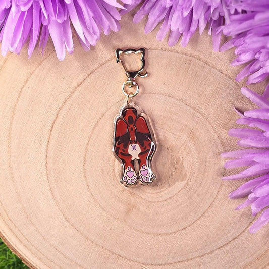Cat-shaped keychain with red design on a wooden surface surrounded by purple flowers