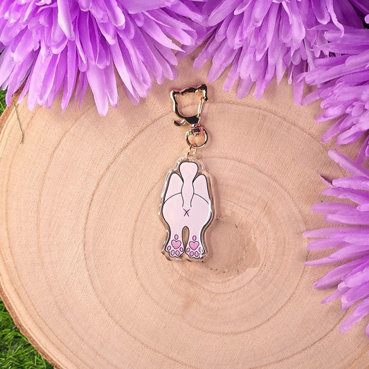 cat keychain charm with a butt design on a wooden surface with purple flowers.