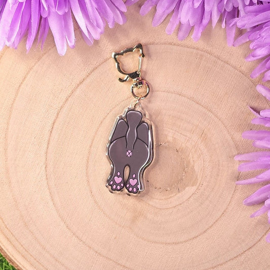 Cat-shaped keychain on a wooden surface surrounded by purple flowers.
