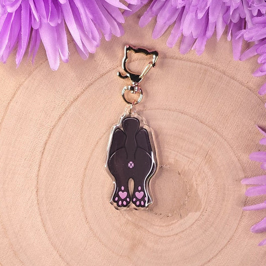 cat butt keychain with a design on a wooden surface surrounded by purple flowers