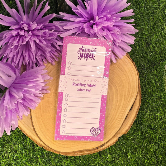Pink 'Positive Vibes' jotted pad with purple flowers on a grass background