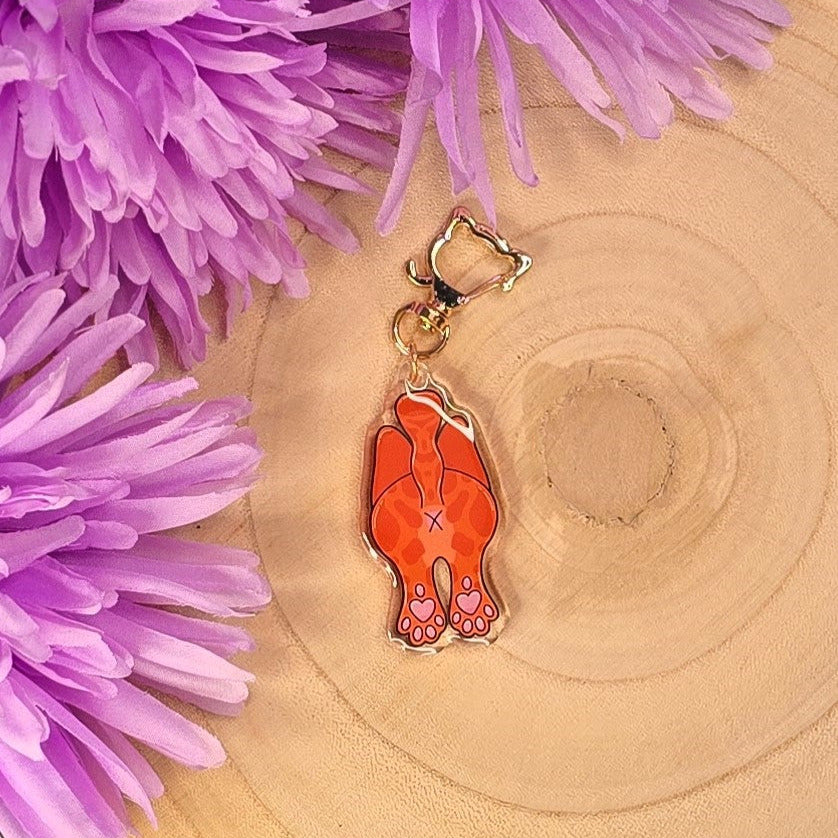 Orange keychain with a cat face design on a wooden surface with purple flowers.
