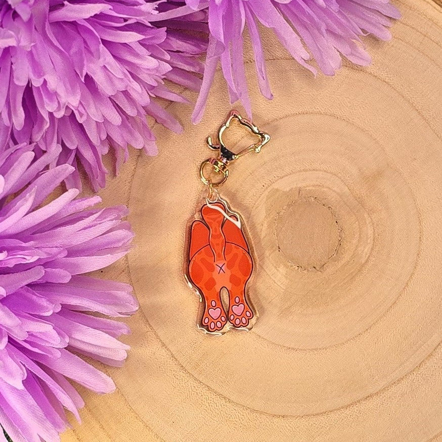 Orange cat-shaped keychain on a wooden surface with purple flowers in the background