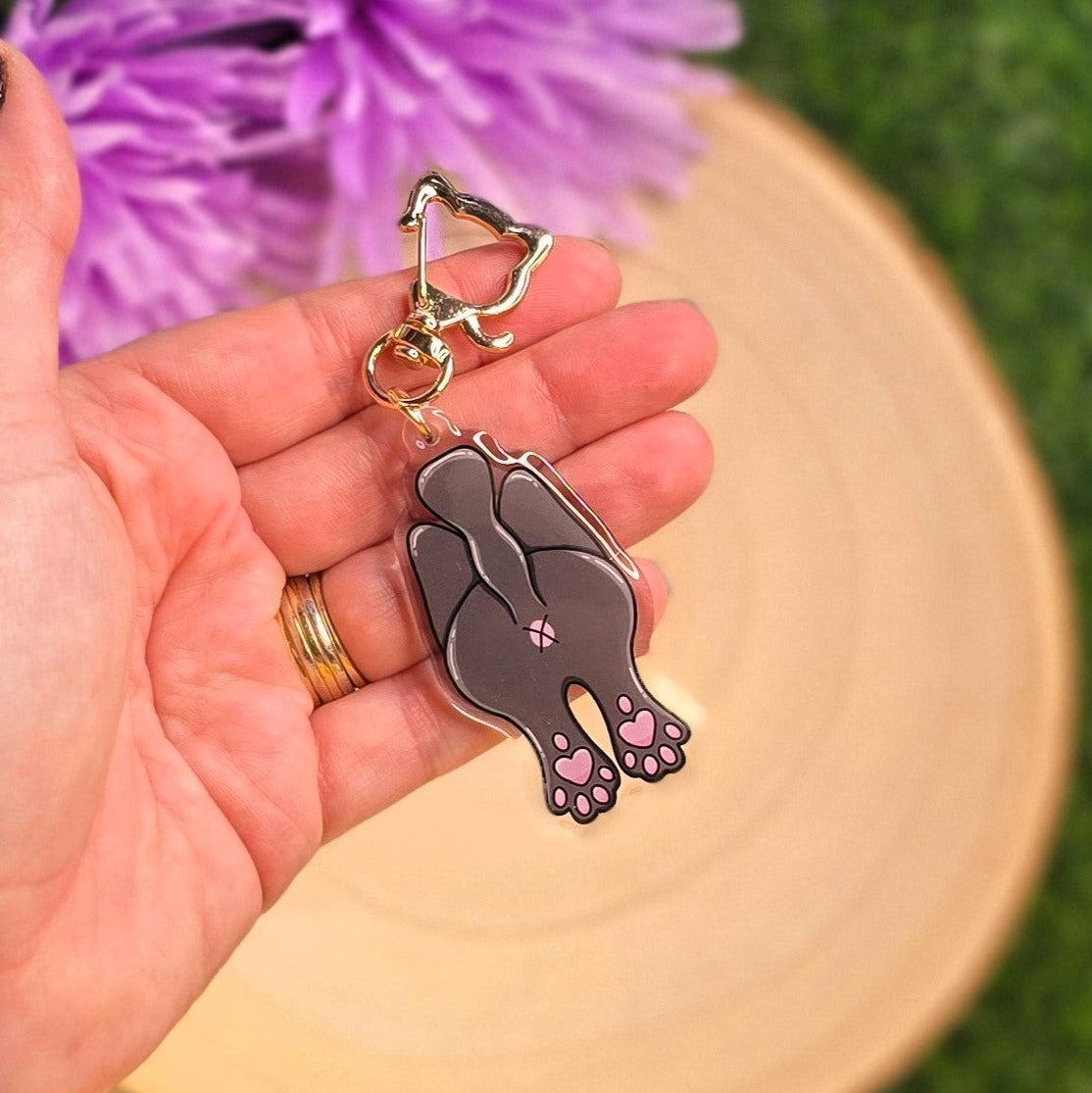 Hand holding a keychain with a cat-shaped charm against a grassy background