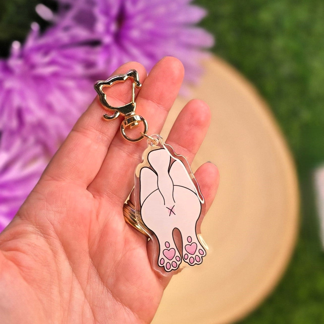 Hand holding a keychain with a cat design against a blurred natural background