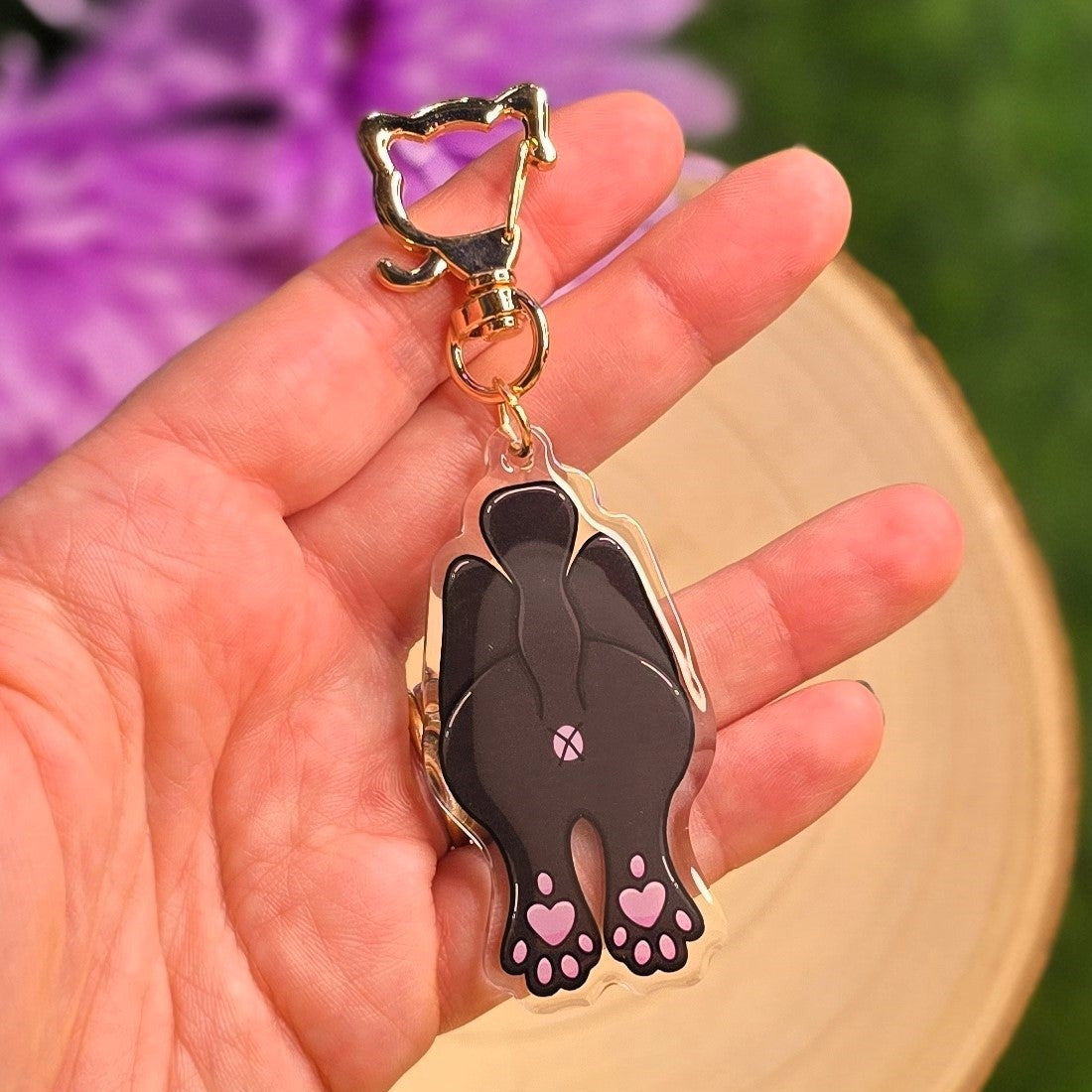 Hand holding a keychain with a black paw design against a blurred natural background