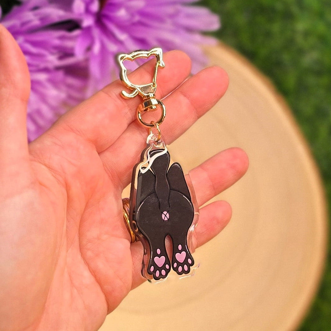 Hand holding a keychain with a black cat design against a blurred natural background