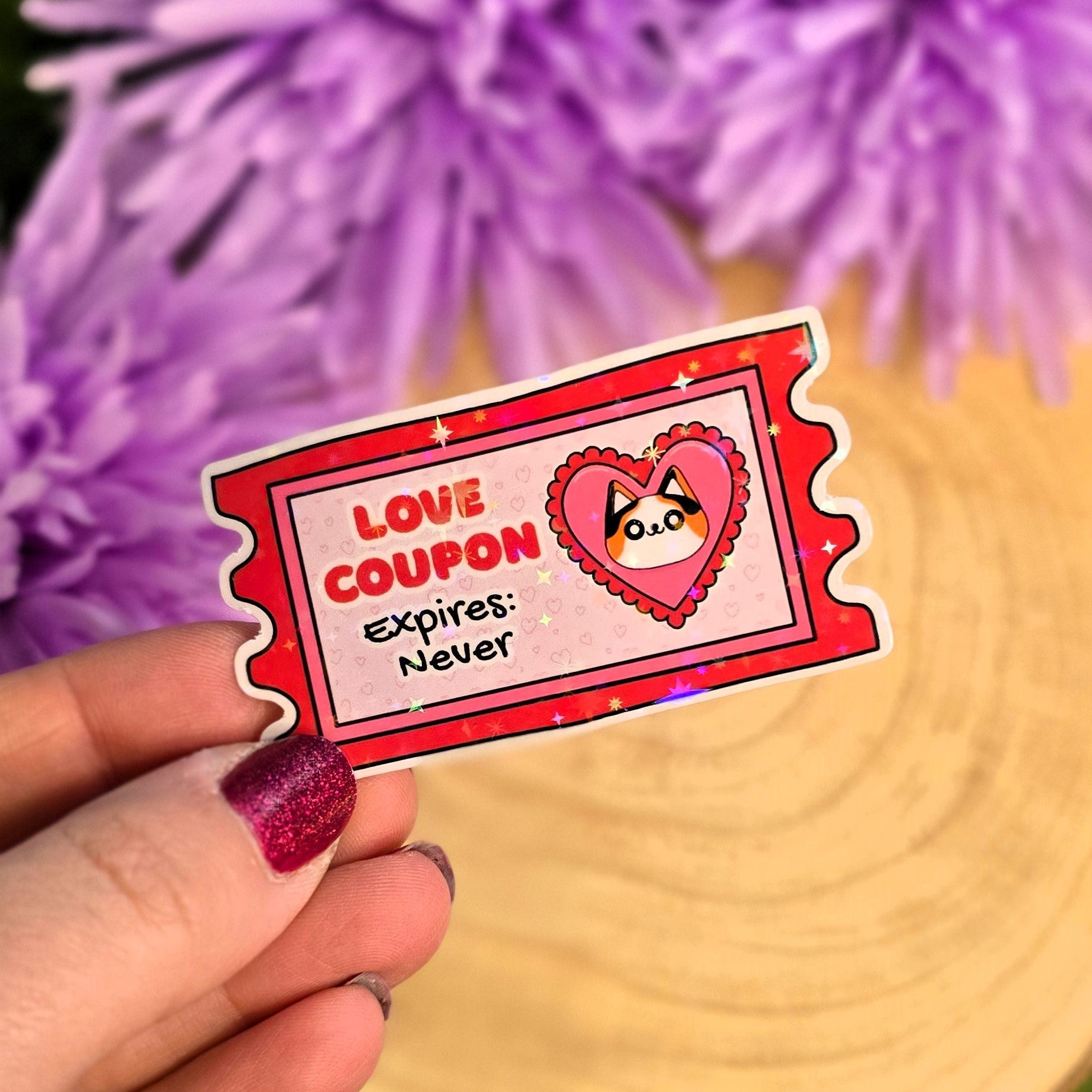 Hand holding a 'Love Coupon Expires: Never' sticker with purple flowers in the background