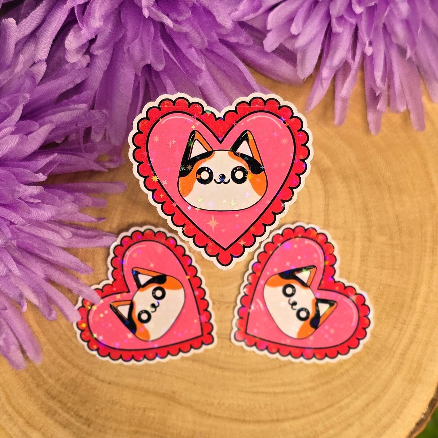 Heart-shaped stickers with cat designs on a wooden surface with purple flowers in the background